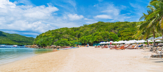 sandy beach on tropical island in a bay by sea on sunny summer day. Luxury resort with beach and sun umbrellas for relaxing in traveling in Asia. Landscape panorama with a view of coast by ocean