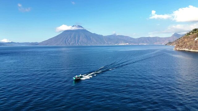 Aerial view of a turquoise boat swiftly slicing through the deep blue waters of Lake Atitlan, leaving white wakes, Lake Atitlan, Guatemala.