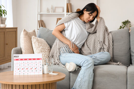 Young woman with plaid suffering from menstrual cramps on sofa at home