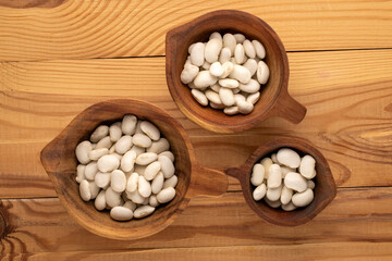 White uncooked beans on a wooden table, close-up, top view.