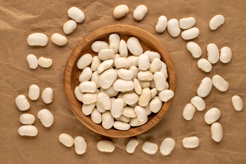 White uncooked beans on kraft paper, close-up, top view.