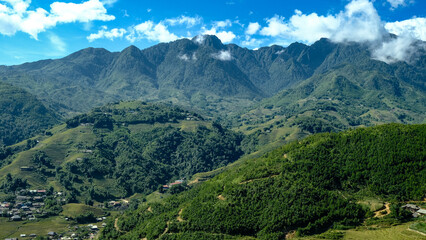 Fototapeta premium ast green mountain valley with terraced fields and scattered villages. Dramatic peaks under a blue sky with clouds. Evokes travel and natural beauty.