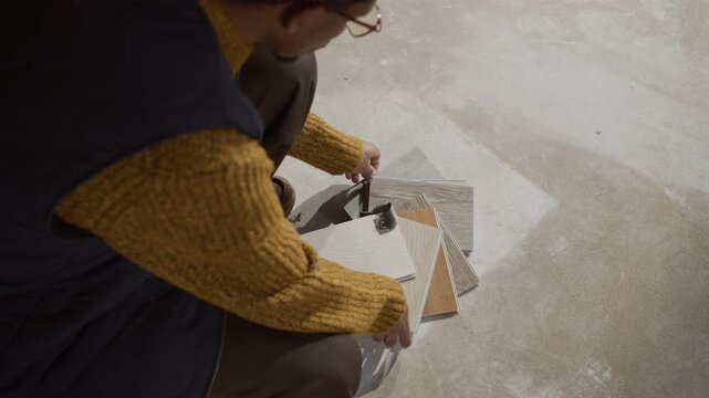 From above shot of African American male interior designer inspecting floor samples at unfinished construction site, planning materials, colors, and layouts for residential or commercial spaces