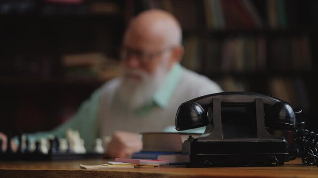 Close-up of retro telephone on grandmaster desk while senior man plays chess
