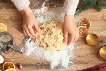 Young woman kneading dough for Panettone on wooden background, closeup. Christmas food concept
