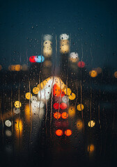 Mesmerizing cityscape at night viewed through a window covered in raindrops, creating a vibrant bokeh of blurred streetlights and a contemplative urban atmosphere