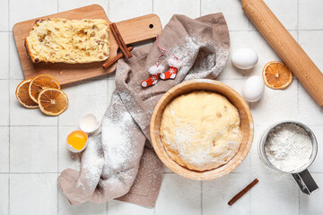 Bowl of dough for Panettone with ingredients and Christmas decor on white tile background