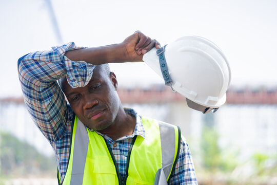 Tired Construction Worker Wiping Sweat on Hot Day,African American Engineer Taking Break from Hard Work at Site,Portrait of a Focused Laborer or Foreman in Safety Gear