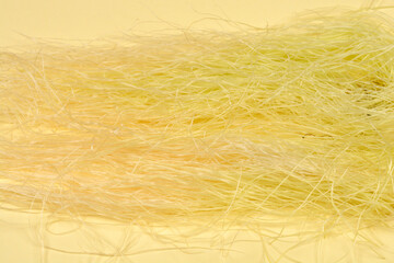 A horizontal close-up shot of light yellow corn silk fibers scattered across a warm, solid pale yellow background, creating a soft and organic texture