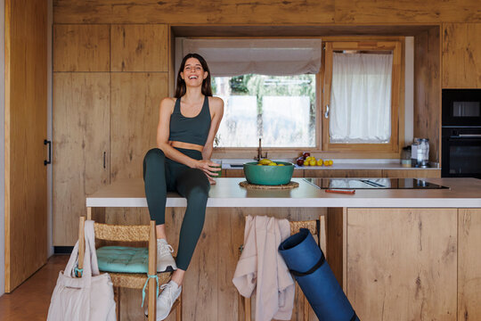 Woman sitting on kitchen counter with yoga mat and green juice in a sustainable home