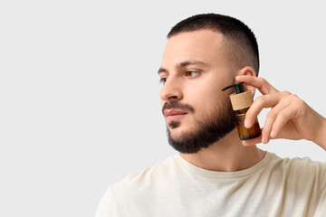 Handsome young man with bottle of vitamin E serum on grey background