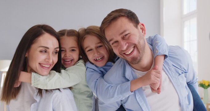 Happy family picture of close smiling laughing young mom and dad posing with cute little daughter, small excited funny girland boy hug happy parents, looking at camera making cute photo together