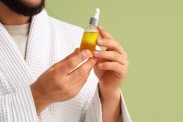 Fototapeta premium Young man with bottle of vitamin E serum on green background, closeup