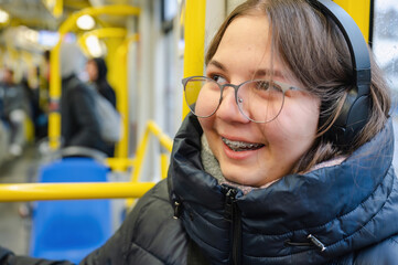 Smiling teenager girl with braces and headphones in tram during rainy weather