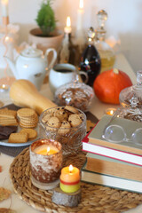 Lit candles, cookies, chocolate, nuts, tea, wine, pumpkins, books, reading glasses and autumn leaves on the table. Autumnal hygge at home. Selective focus.
