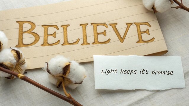 Inspirational message with the word believe on a note beside cotton flowers on a soft fabric background
