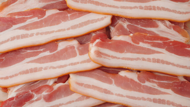 A close-up photograph of strips of raw bacon arranged as a textured background pattern. The bacon strips display marbled pink and white fat streaks with deep red meat portions, creating natural organi