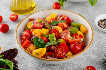 A salad of farm-fresh multi-colored tomatoes, red onions and fresh basil in a bowl on a gray concrete background. Healthy food. Top view.