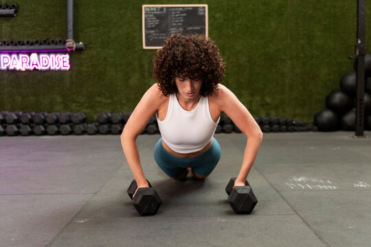 Focused woman practicing dumbbell push-ups at gym