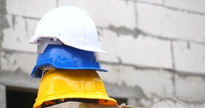 Stack of Safety:  A close-up captures a stack of hard hats of white, blue and yellow, each poised atop the other, positioned against a background of construction blocks.