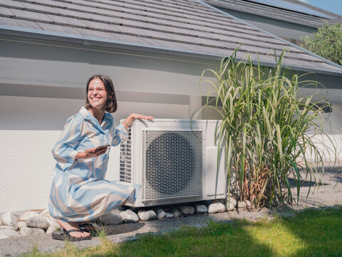 Woman kneeling outdoors checking thermal heat pump with smartphone app