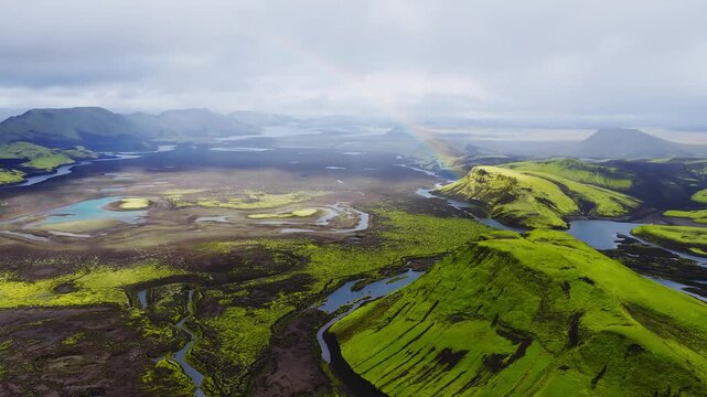 Aerial view moves forward across moss hills, black lava plains, turquoise lakes, and braided rivers near Landmannalaugar and Sigoldugljufur under soft overcast light.