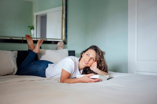 Woman relaxing on bed reading a book in a cozy bedroom at home