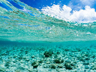 Fototapeta premium 嘉比島の白砂ビーチの半水面撮影。沖縄特有の双胴船サバニや観光客、パラソル、テントが見える。美しいサンゴ礁と熱帯魚の群れ。 安室島沖縄県 島尻郡慶良間諸島座間味島-2025 サンゴの産卵があり卵が漂う。沖縄本島から40km西方の諸島。30以上の島嶼群全体が国立公園に指定。珊瑚礁の青い海と白い砂浜は世界屈指の美。貴重な動植物が多数生息。 