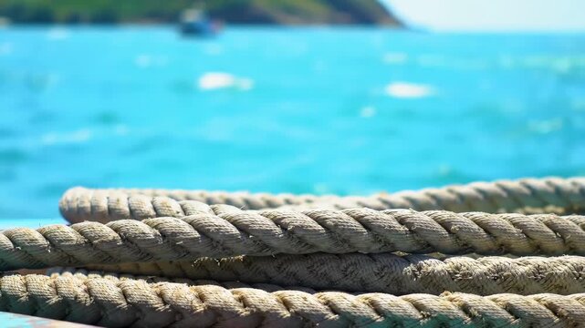 Close-up of nautical rope at dock with ocean and boat background; for travel imagery