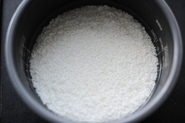 White rice in a rice cooker covered in water ready for boiling as food ingredient