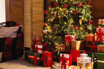 Decorated Christmas tree with many gifts, folding screen and armchair near brown wall in living room at night