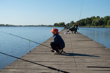 A boy sits on a wooden bridge and fishes