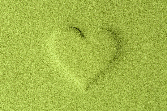 Raised heart shape formed in vibrant green matcha powder creates a minimalist symbol of love, health, and natural energy.