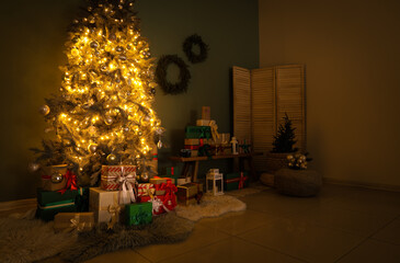 Decorated Christmas tree with glowing lights, many gifts and wreaths in living room at night