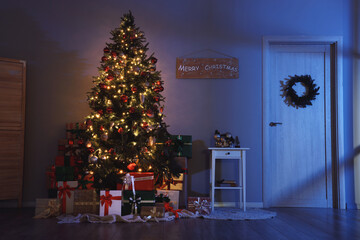 Decorated Christmas tree with glowing lights, many gifts and coffee table in living room at night