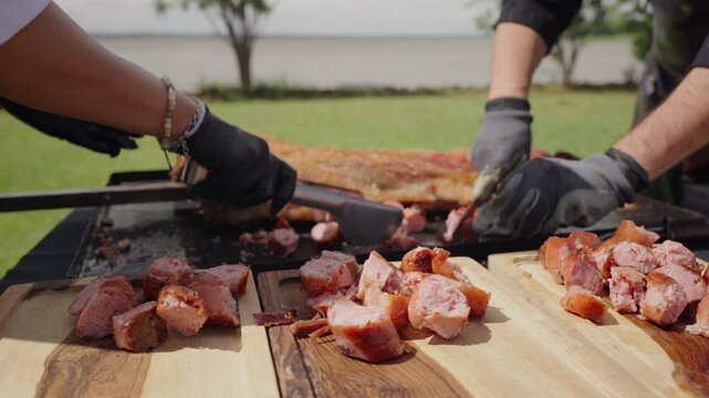 Chef slicing grilled meat and sausages on wooden board during traditional Argentinian asado