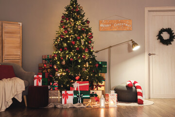 Decorated Christmas tree with many gifts, glowing lamp and armchair in living room