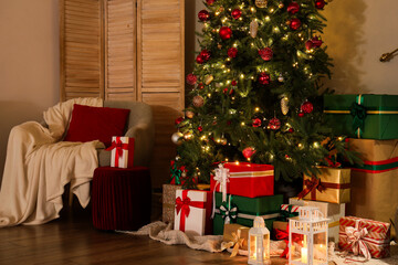Decorated Christmas tree with glowing lights, many gifts and armchair in living room