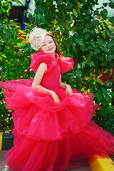 A girl in a lush pink dress and hat near the green bushes