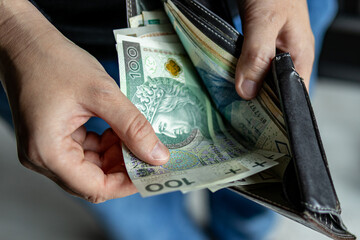 Person pulling out 100 Polish złoty banknotes from a leather wallet. Concept of payment, budgeting, salary or expenses