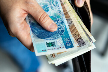 Close-up of a hand holding Polish złoty banknotes taken from a black wallet. Concept of finance, salary, savings, or payment