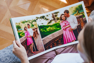 woman is holding and flipping through a photo book with a pregnancy photo shoot