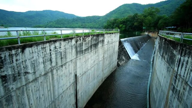 Spillway of a Concrete Weir Dam in Thailand, Contrasting Water Infrastructure with Lush Tropical Green Mountains.