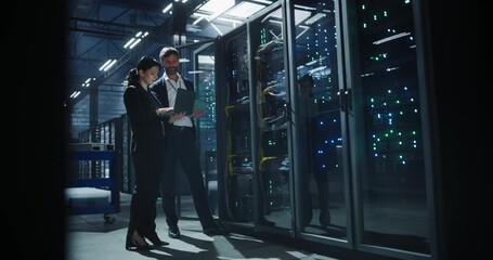 Technicians collaborate in a data center, discussing server rack performance and inspecting hardware connections. Rows of illuminated servers and organized cabling, network monitoring - Powered by Adobe