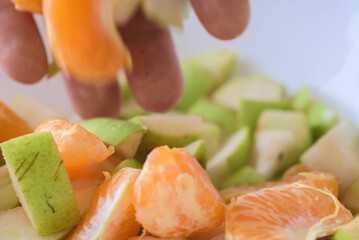 Process of making colorful fruit salad with apples and tangerine. Hand adds tangerine segments to fresh chopped pear fruit salad
