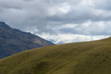 Fototapeta premium Golden tussock ridge with snow covered peaks under dramatic sky, South Island New Zealand 