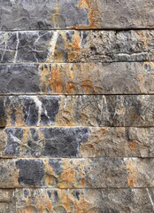 Natural Stone Wall Texture. Close-up of a natural stone wall with rusty streaks and mineral marks. Grey and ochre tones form a rugged background ideal for architecture, design, and texture projects.