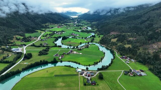 Explore the stunning landscape of Stryn, Norway, featuring vibrant green fields, winding rivers, and picturesque valleys under a dramatic sky. Nature thrives in this serene environment.