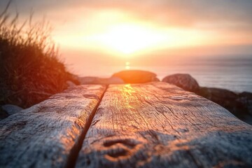 sunset over the ocean viewed from a weathered wooden surface with grasses and rocks in the background evoking calm and tranquility