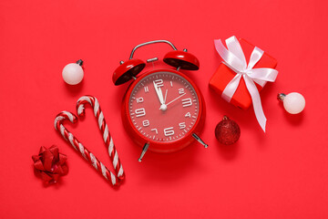 Obraz premium Alarm clock with Christmas decorations and gift box on red background